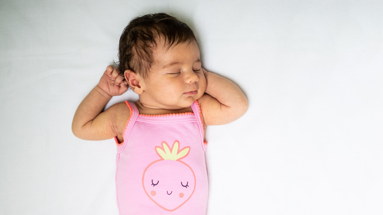 A baby sleeps on their back in a crib.